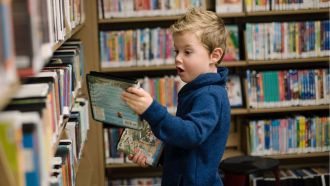Child makes an excited face as they pull an item from a library shelf