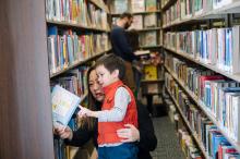Woman helps young boy choose a library book.
